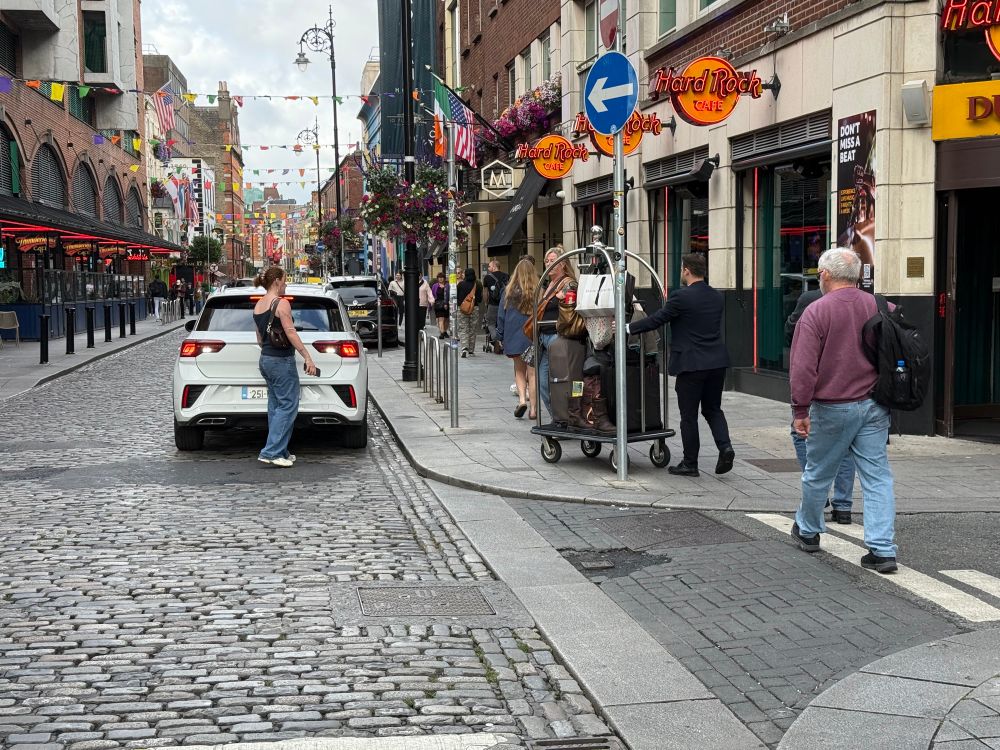 Photo of hotel doorman wheeling luggage to a taxi parked away from the hotel.