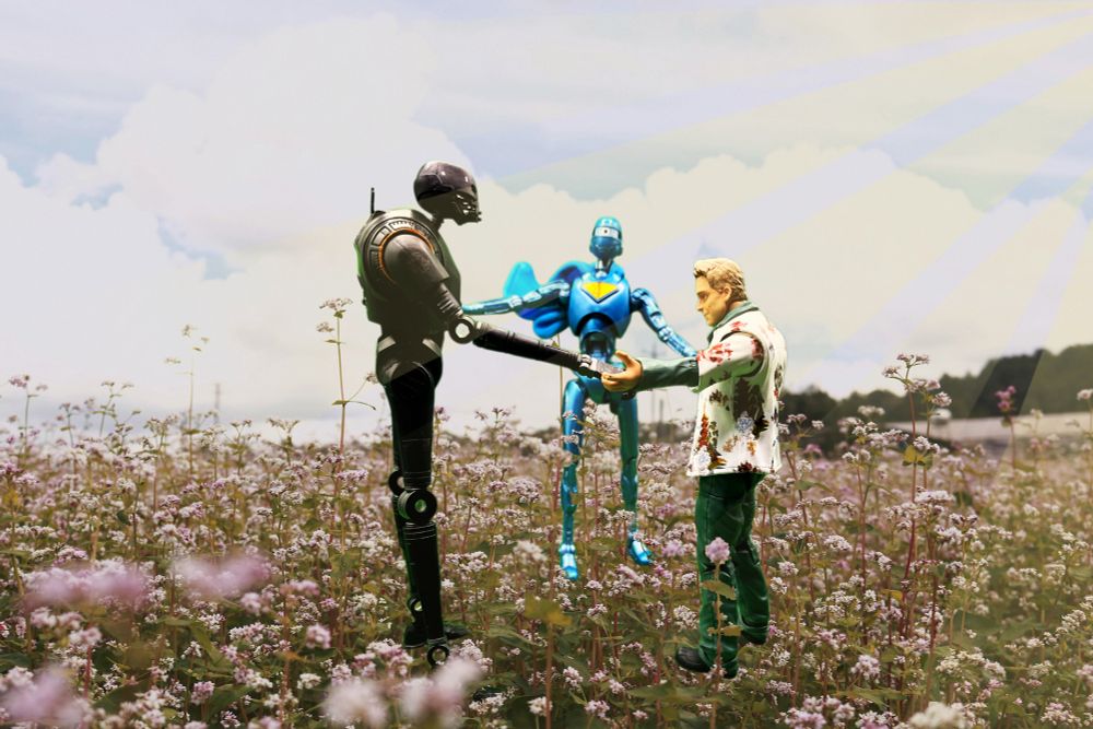 In a field of flowers, Wash from Firefly, K2SO from Andor, and Robot #4 from Superman stand in a circle, holding hands in the sun, as Robot #4’s cape billows to his left.