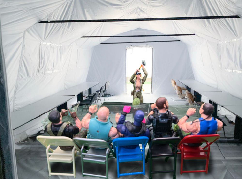 In a big white military tent, Cover Girl stands behind a table, sledgehammer raised over her head, about to smash a watermelon. In a row of folding chairs, Flint, Gung Ho, Snake Eyes, Breaker, and Sgt. Slaughter hold a clear plastic tarp up in front of them to fend off the imminent splatter.