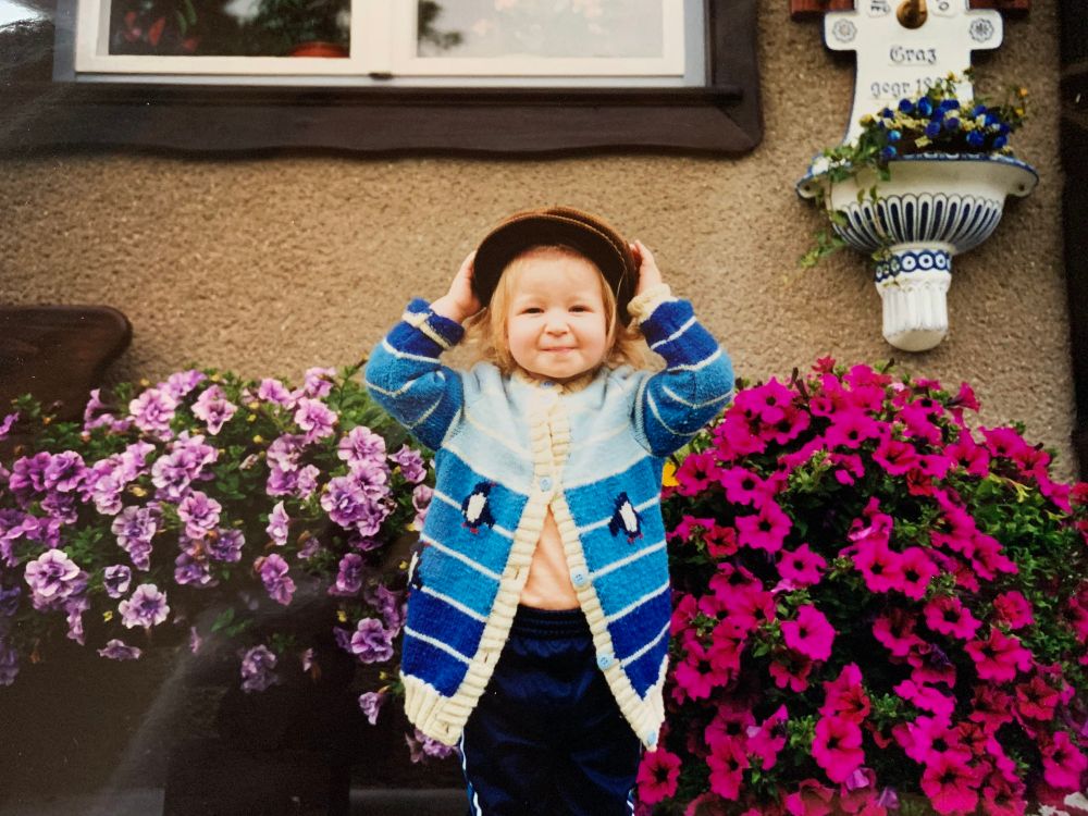DasLieschen as a toddler, wearing a cap and a handmade cardigan with blue stripes and two penguins.
