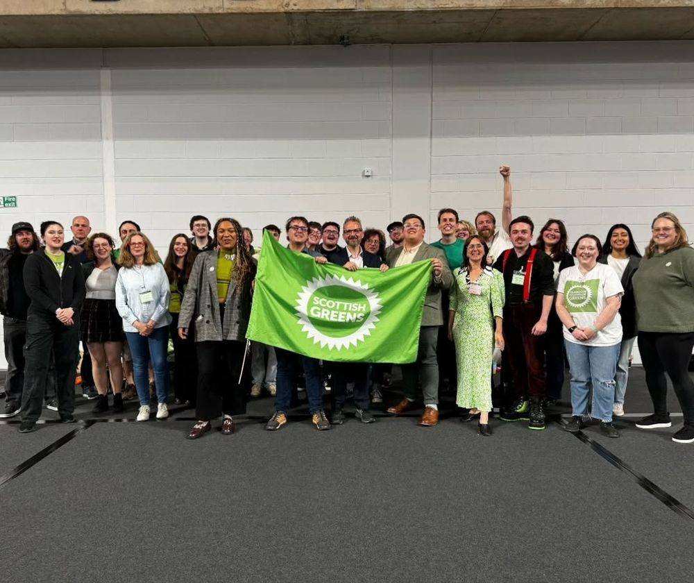 Glasgow greens smiling to camera in a big hall, with a green flag