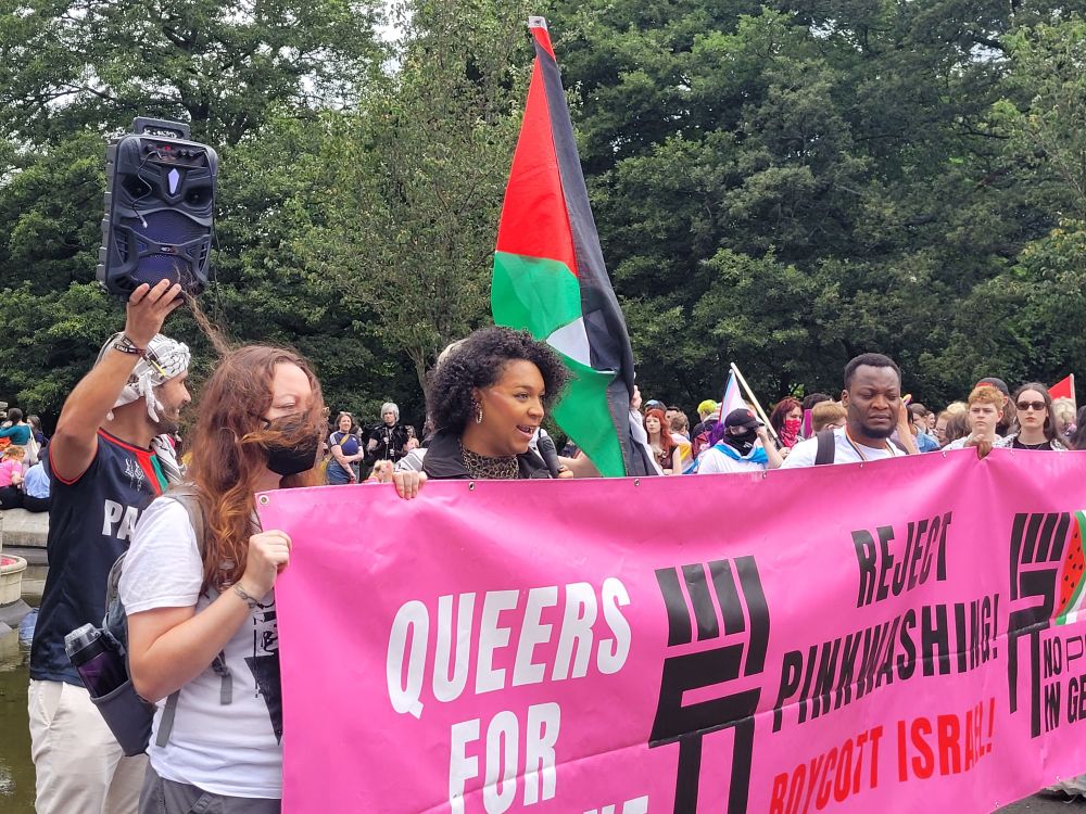 Iris Duane speaks behind a no pride I  genocide pink banner