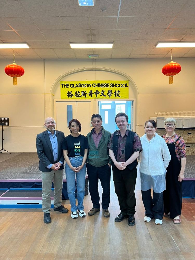 Photo of Patrick & Anthony with members of the Chinese School, standing under a banner for the school and smiling to camera.