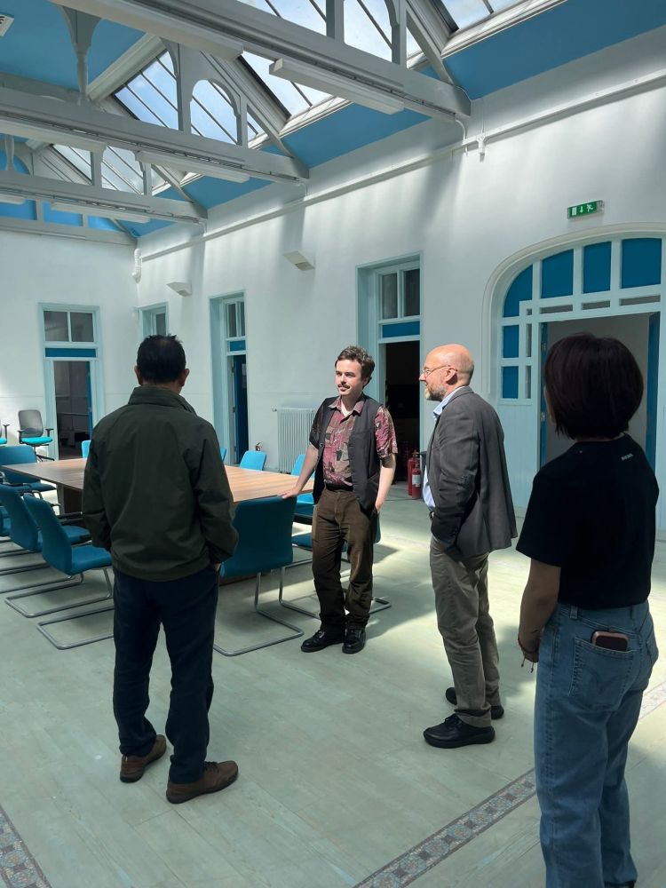 Anthony & Patrick in a well lit roof room with Sam & Po backs to camera, talking to each other.