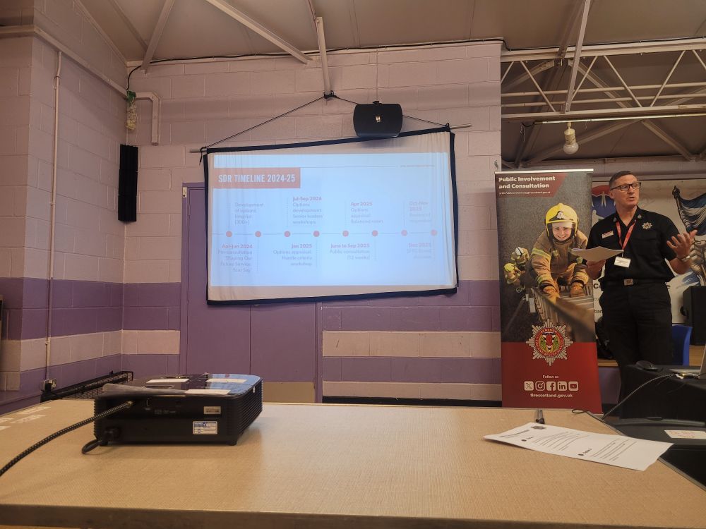 PowerPoint on a screen with fire service staff standing beside talking 