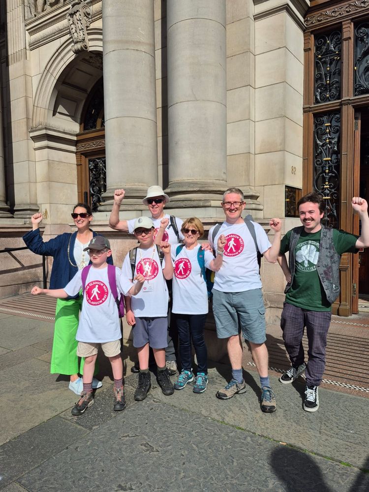 Deputy Lord Provost Christy Mearns (left) and Anthony (right) welcome the Glasgow Way walkers to the City Chambers as they end their walk there, with all smiling to camera with fists waved in the air 