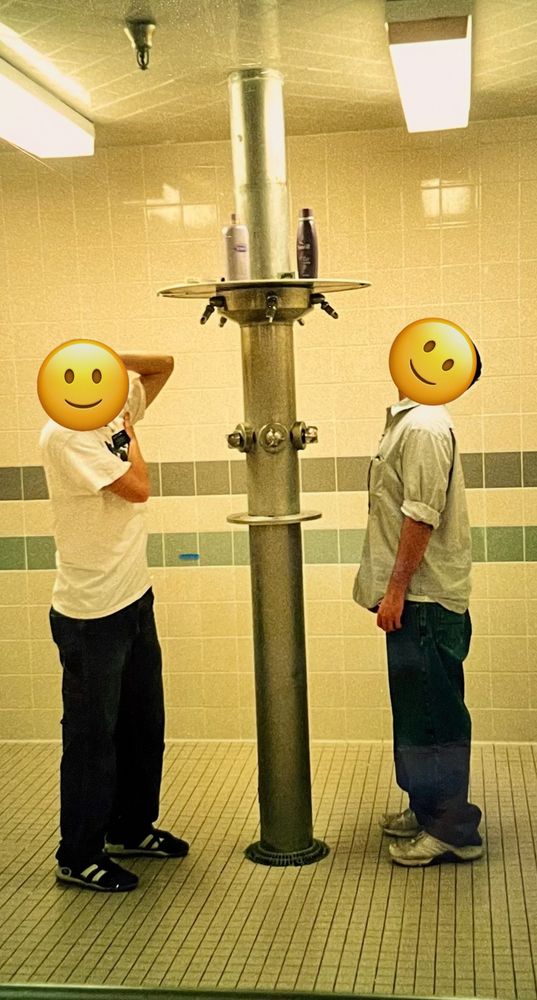 Two Mormon missionaries fully clothed in normal clothing during a cleaning assignment are pictured pretending to shower at one of the group showers.