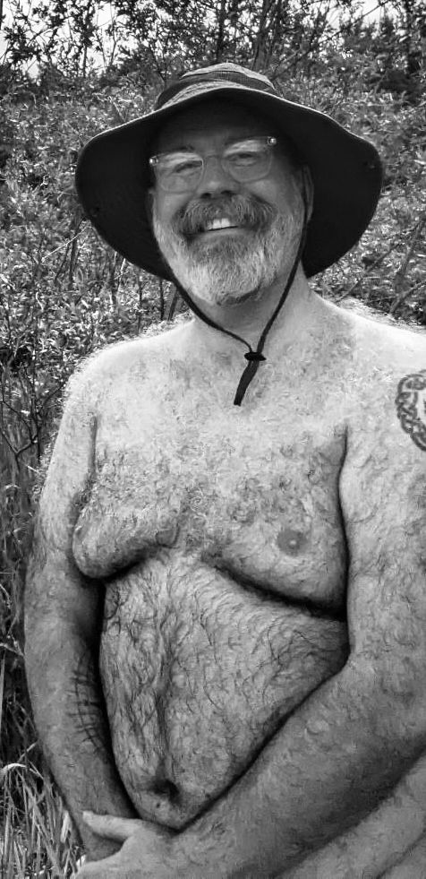 Waist up pic of a hairy bear dad in glasses wearing an outdoor hat. 