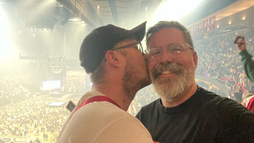 Boy in hat and glasses kissing dad at the Charli XCX concert