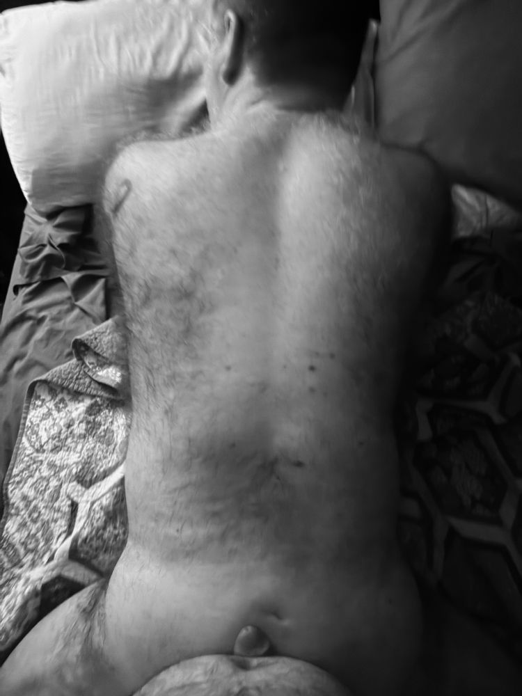 Hairy man laying face down on bed