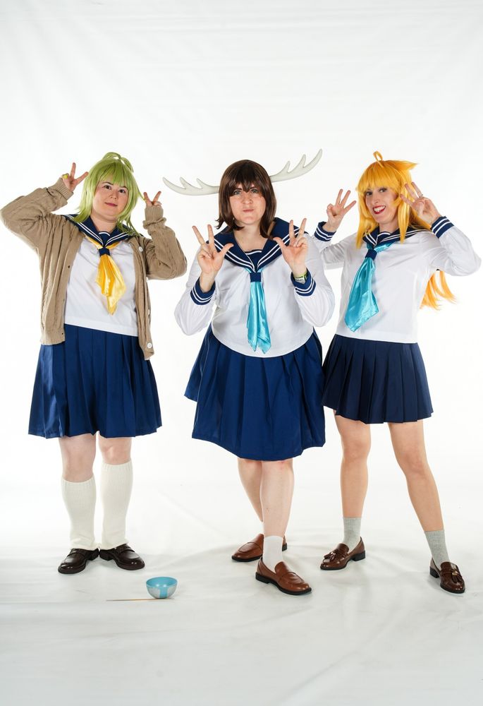 Three cosplayers dressed up in school uniforms as characters from the anime My Deer Friend Nokotan: Bashame, Noko Tan, Koshi Tan
