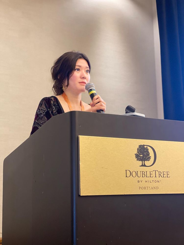 Irene listening to attendee share, as she stands with a microphone in both hands.