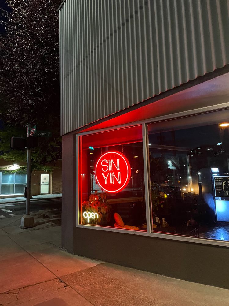 Storefront has 2 neon signs. One red sign says Sin Yin. The white sign says open.
