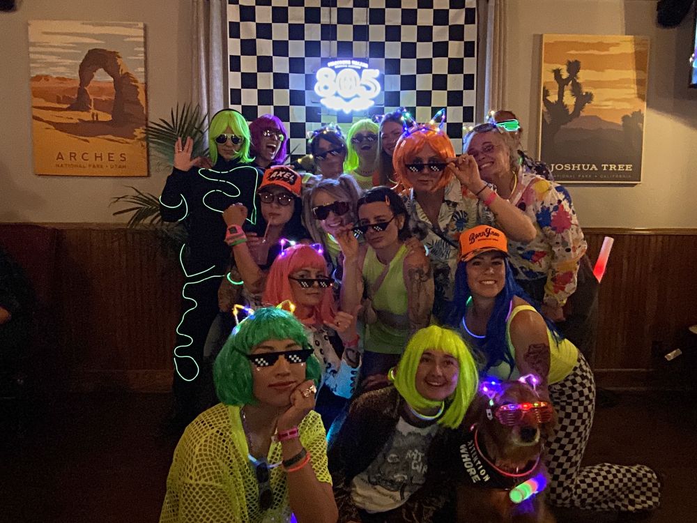 A group of women dressed in neon taking a group photo in front of the 805 checkered backdrop 