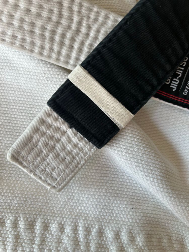 A close up shot of a white gi with a white belt sitting on top. The belt has one white stripe.  