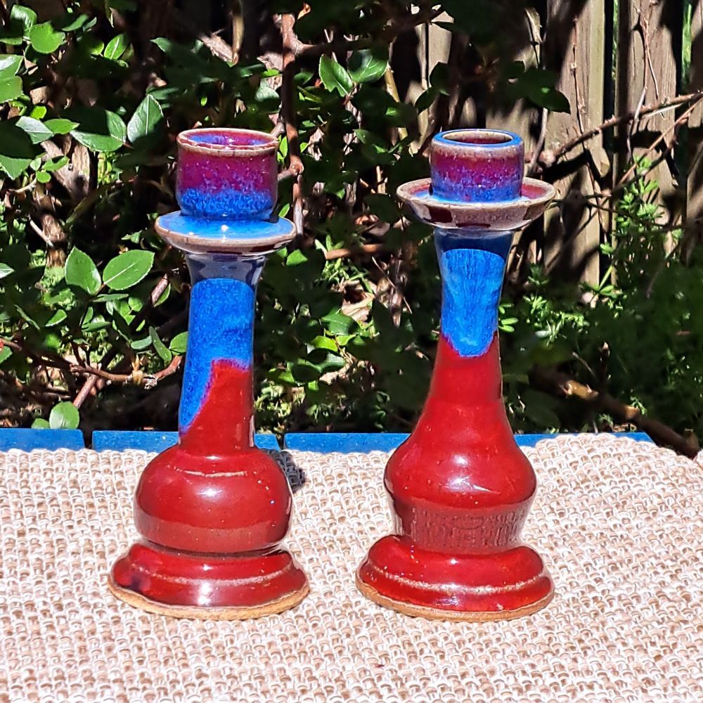 A pair of stoneware candlesticks, glazed in red with a multishade blue layered and dripping over the red. 