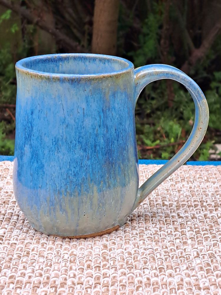 A stoneware mug. It is glazed in blue streams of color over pale green.