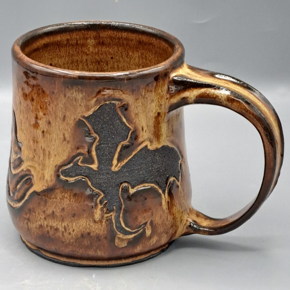 A mug made of black clay and glazed in golden/bronze. A dragon blowing flames is carved and resisted in raw black clay