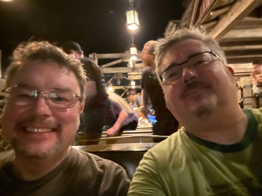 Two gentleman seated in the back row of their boat, Pirates of the Caribbean.  