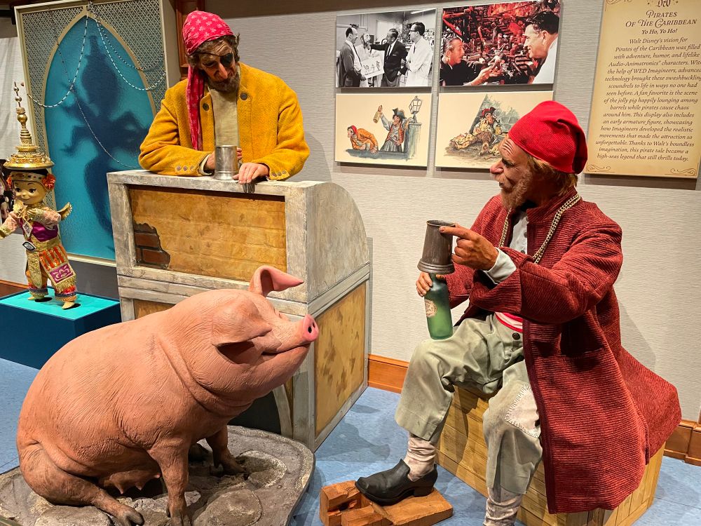 A series of figures, including a pirate standing behind a crate, a pirate seated on a crate, and a pig, from Pirates of the Caribbean.  Non functional animatronics.  