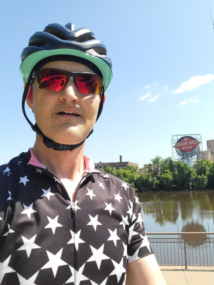 Me, across the river from the Grain Belt sign, wearing a cycling kit inspired by the stars painted on the exterior of First Avenue