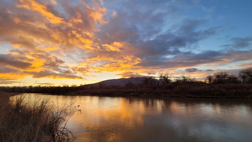 The Rio Grande at dawn with the clouds illuminated and the clouds also reflected in the surface of the river.