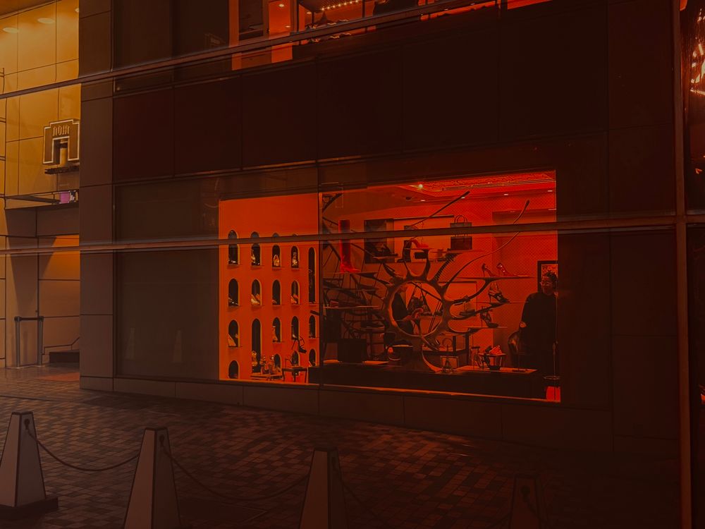 A picture of the Louboutin storefront in Gina, Tokyo reflects in a red glow on the building beside it. 