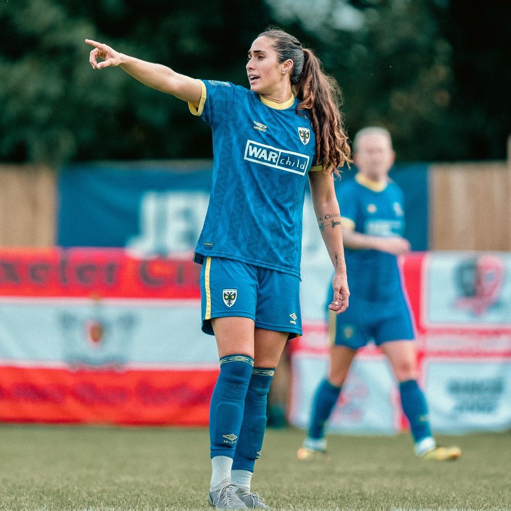 Footballer Kau'inohea Solomon-Taylor is in a blue football kit, pointing towards her right and calling out. 