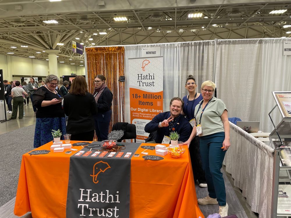 Group of people standing in front of a trade show booth with a tablecloth that reads HathiTrust 