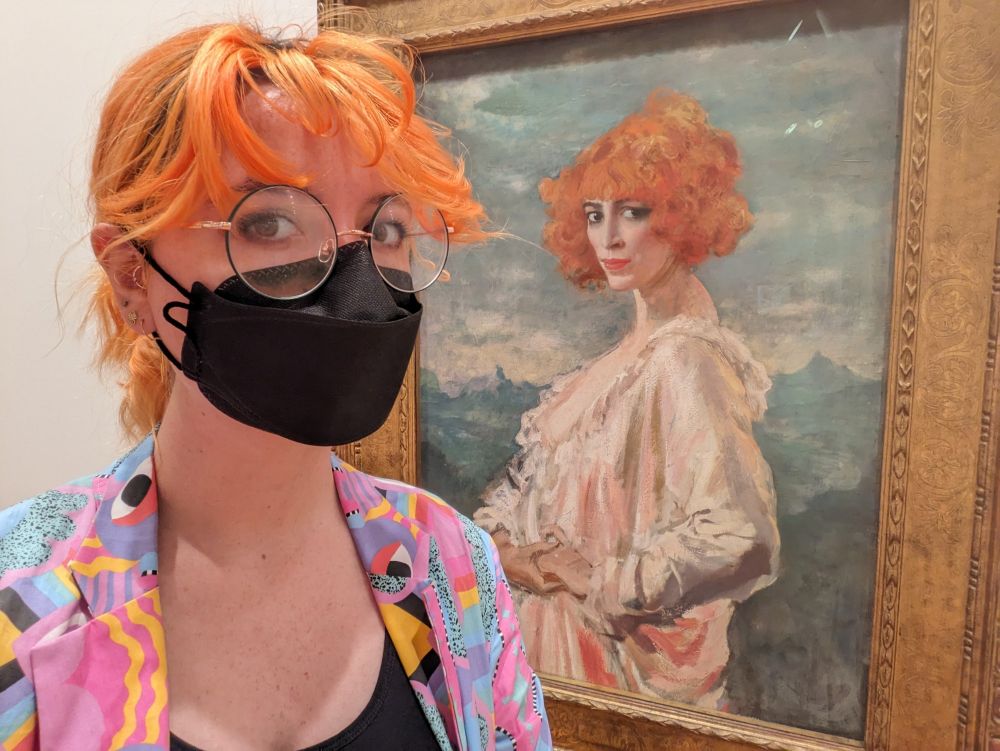 Self portrait with orange curly hair on front of a painting of a woman with orange curly hair