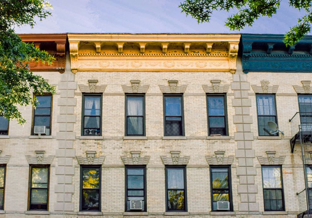 Three limestone Victorian row houses—one with a cornice painted red, another off-white, and the third blue 