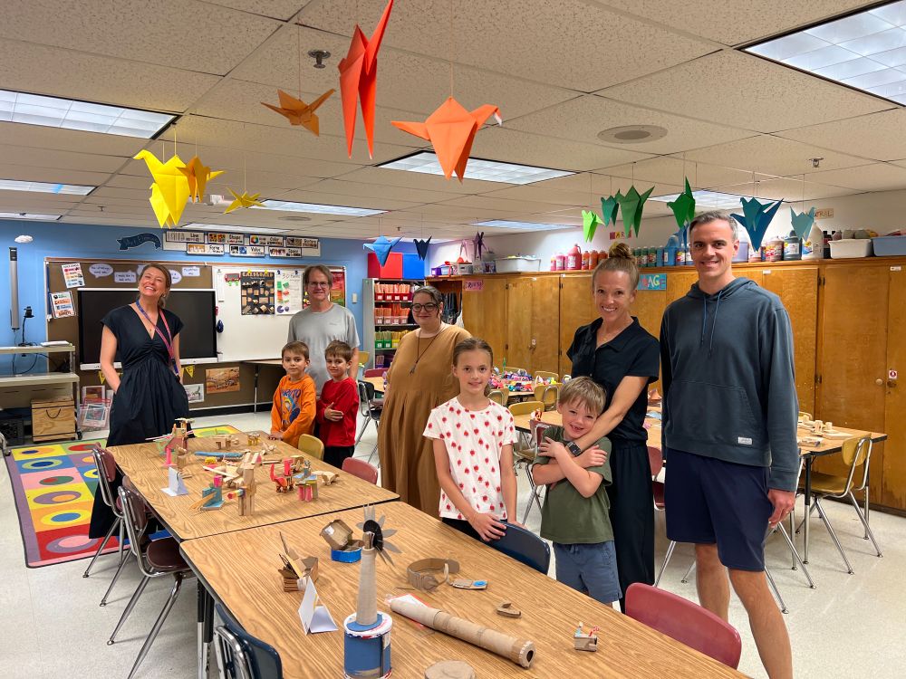 Art teachers, students and parents stand by table with artwork 