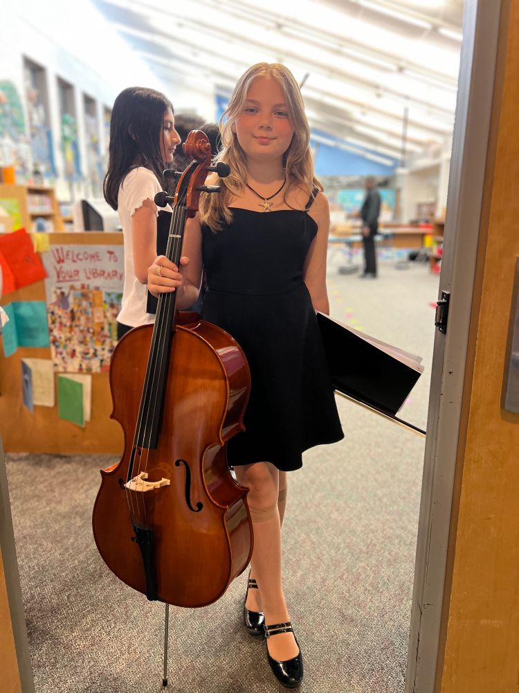 Students warmed up in the library before the performance. Students stands in line holding cello 