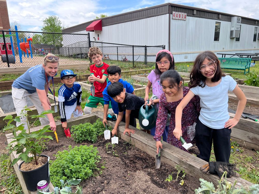 Science Coach Carrie Lombardi with students holding trowels shovels and watering can
