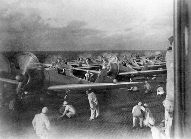 planes on the deck of an aircraft carrier lined up with crew around them 