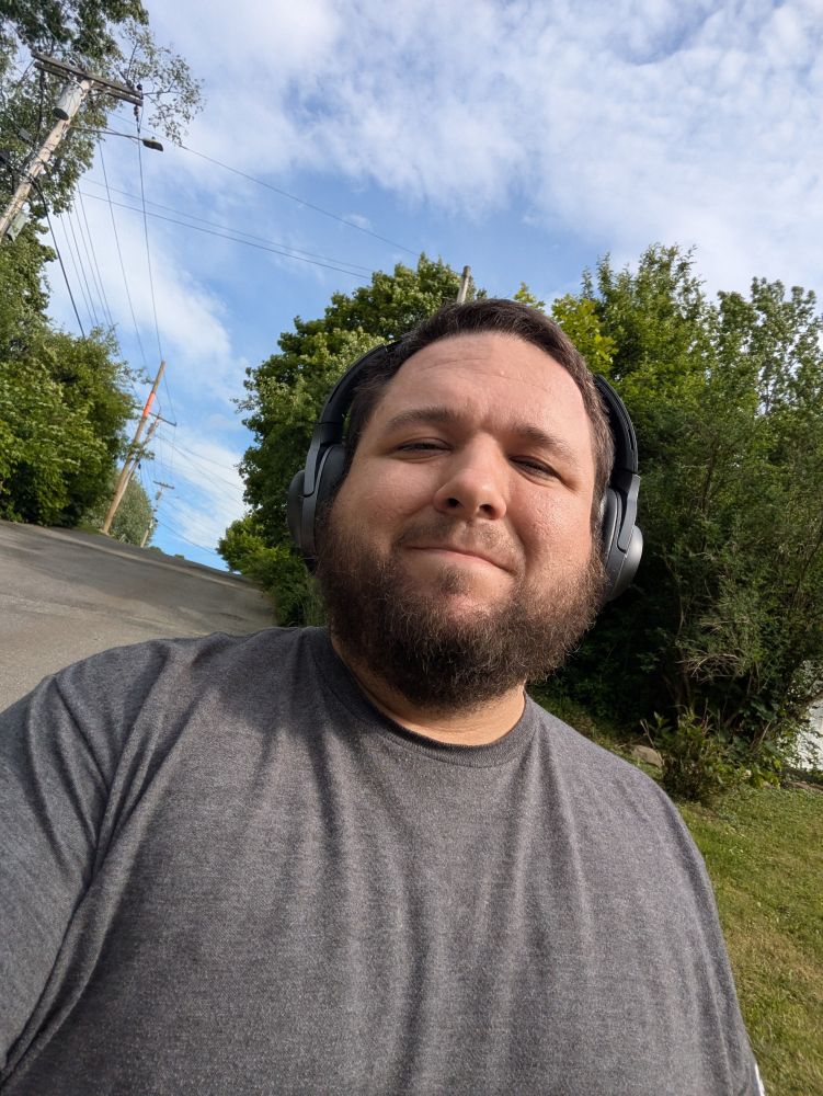 Selfie of me standing in the sun. I'm smiling and wearing headphones 