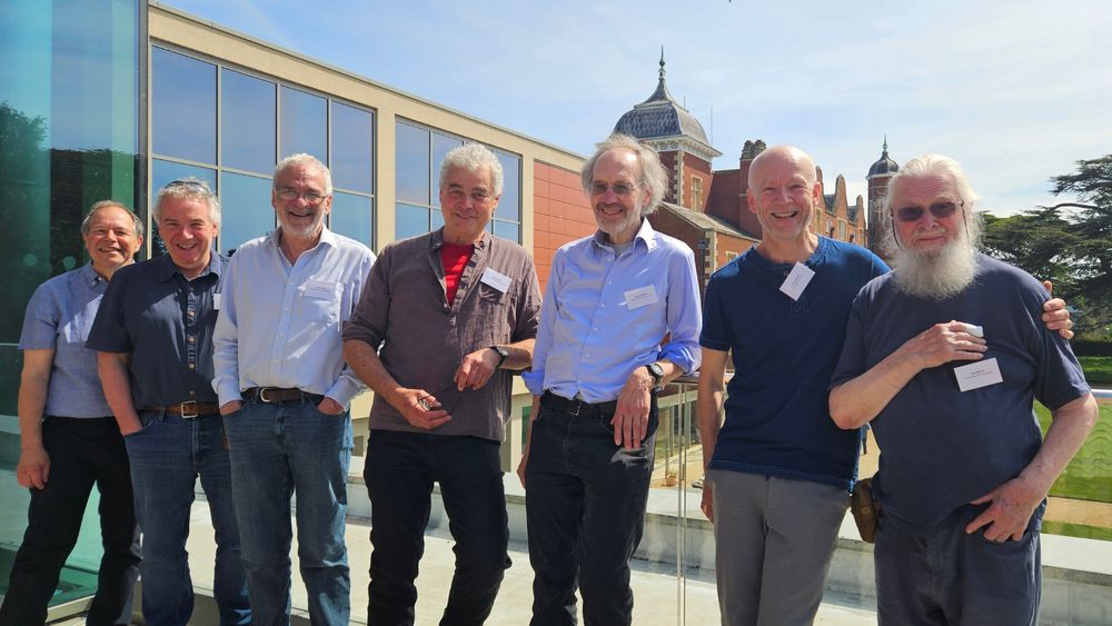 A group of 8 people gathered together outside with a backdrop of the Babraham Research Campus. From left to right: Phill Hawkins, Peter Cullen, Robin Irvine, Peter Parker, Roger Williams, Len Stephens and Bob Mitchell.