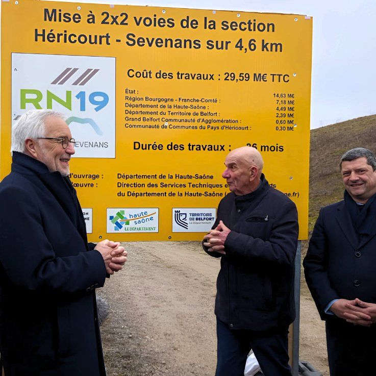Yves Krattinger, président du conseil départemental de la Haute-Saône, accompagné de Florian Bouquet, président du département du territoire de Belfort, détaille au ministre François Rebsamen le projet de travaux de la Route nationale 19. Un tableau jaune récapitulant le chantier et ses acteurs se dresse en fond.