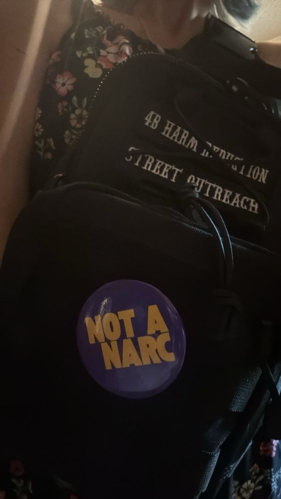 Black leather jacket and bag with Not a Narc pin