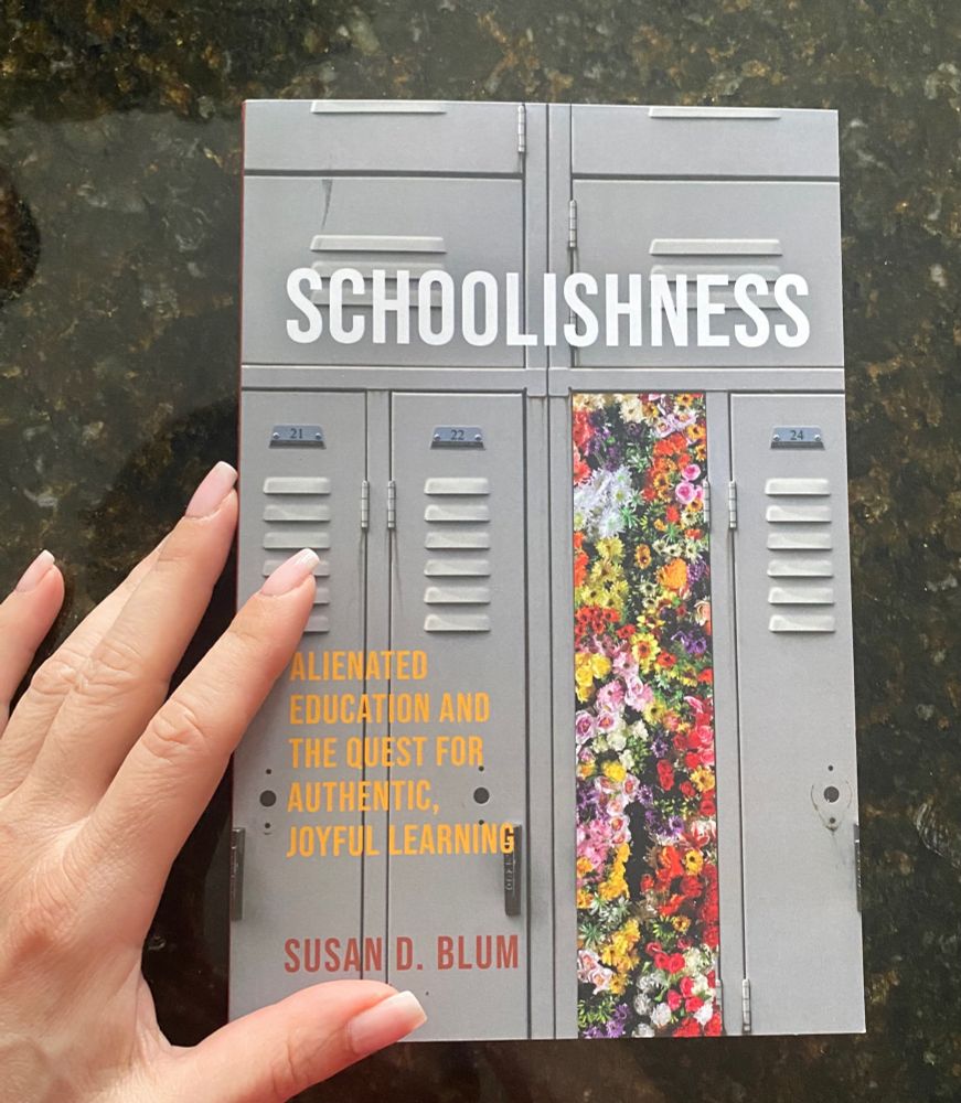 Book cover with title Schoolishness in white letters. Subtitle in yellow letters, Alienated Education And The Quest For Authentic, Joyful Learning. Author’s name in reddish-brown letters Susan D. Blum along the bottom. Grey background of four school lockers numbered twenty one to twenty four. Third locker covered in multicoloured flowers. White woman’s left hand on left side pointing to book cover.