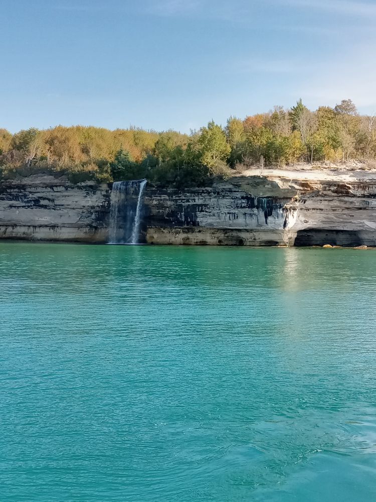 Bright blue green waters of Lake Superior and cliffs topped with fall colored trees. Pictured Rocks Lake shore near Munising, MI