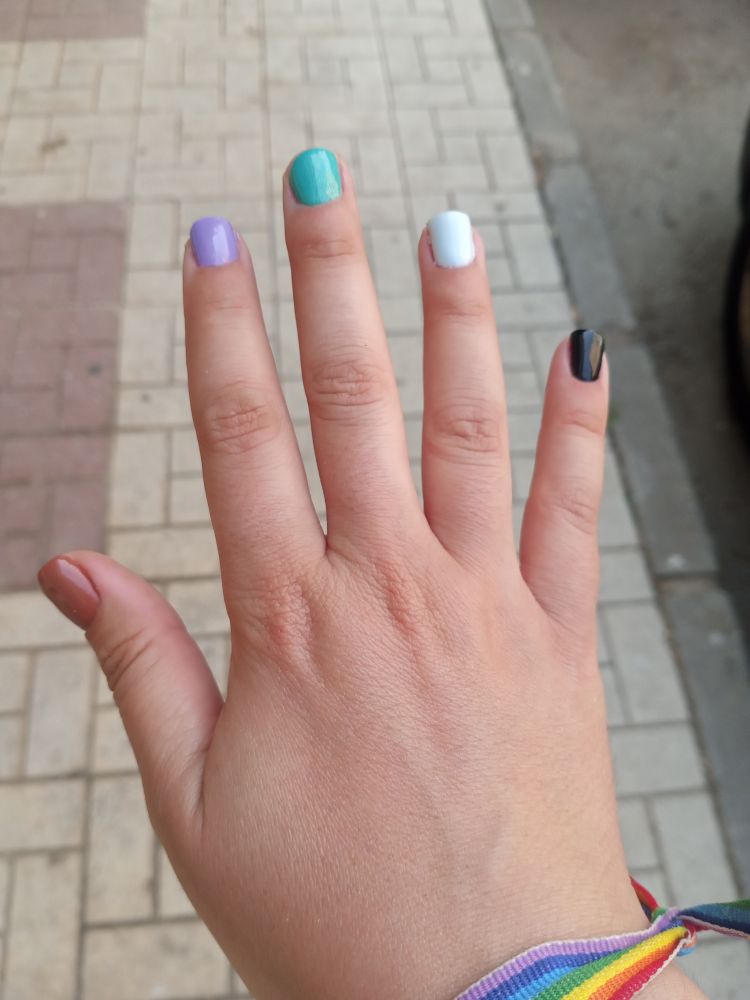 Foto de mi mani derecha, enseñando las uñas con un color diferente en cada dedo. De izquierda a derecha: marrón claro, lila, azul turquesa, blanco azulado y negro