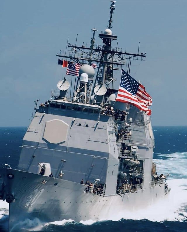 Ticonderoga-class guided missile cruiser USS NORMANDY (CG 60) turns at high speed while flying the “battle ensign,” an inspiringly large American flag. 