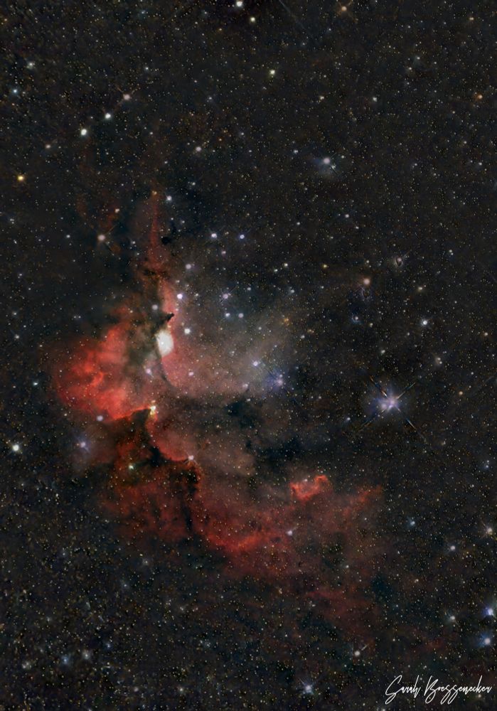 A red and orange nebulosity in a field of multi-colored stars that is vaguely shaped like a wizard - his hat and nose are at the top of the image