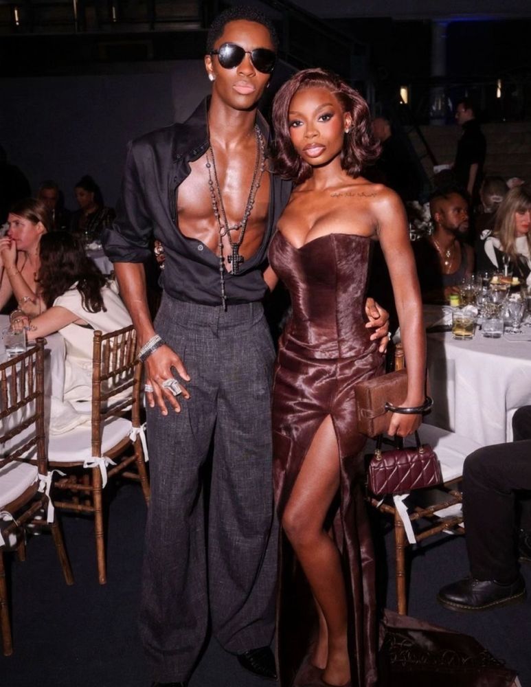 Alton Mason and Olandria Carthen at the 2025 CFDA Fashion Awards. Alton is wearing a black opened up button down shirt with grey high waisted pants and Olandria is wearing a Brandon Blackwood brown suede gown with a matching purse
