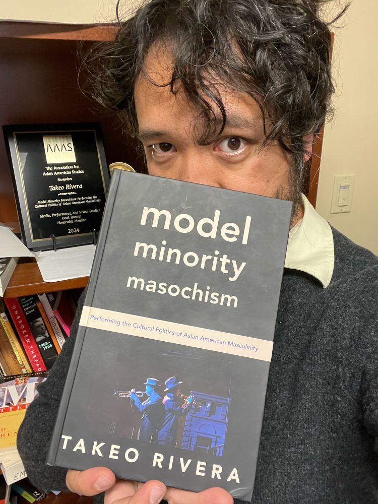 Asian guy holding up his book to obscure half his face