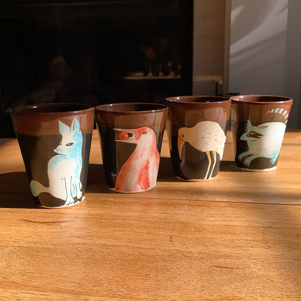 Handmade tumblers with a fox, a raven, another raven and a racoon, all painted with underglaze.