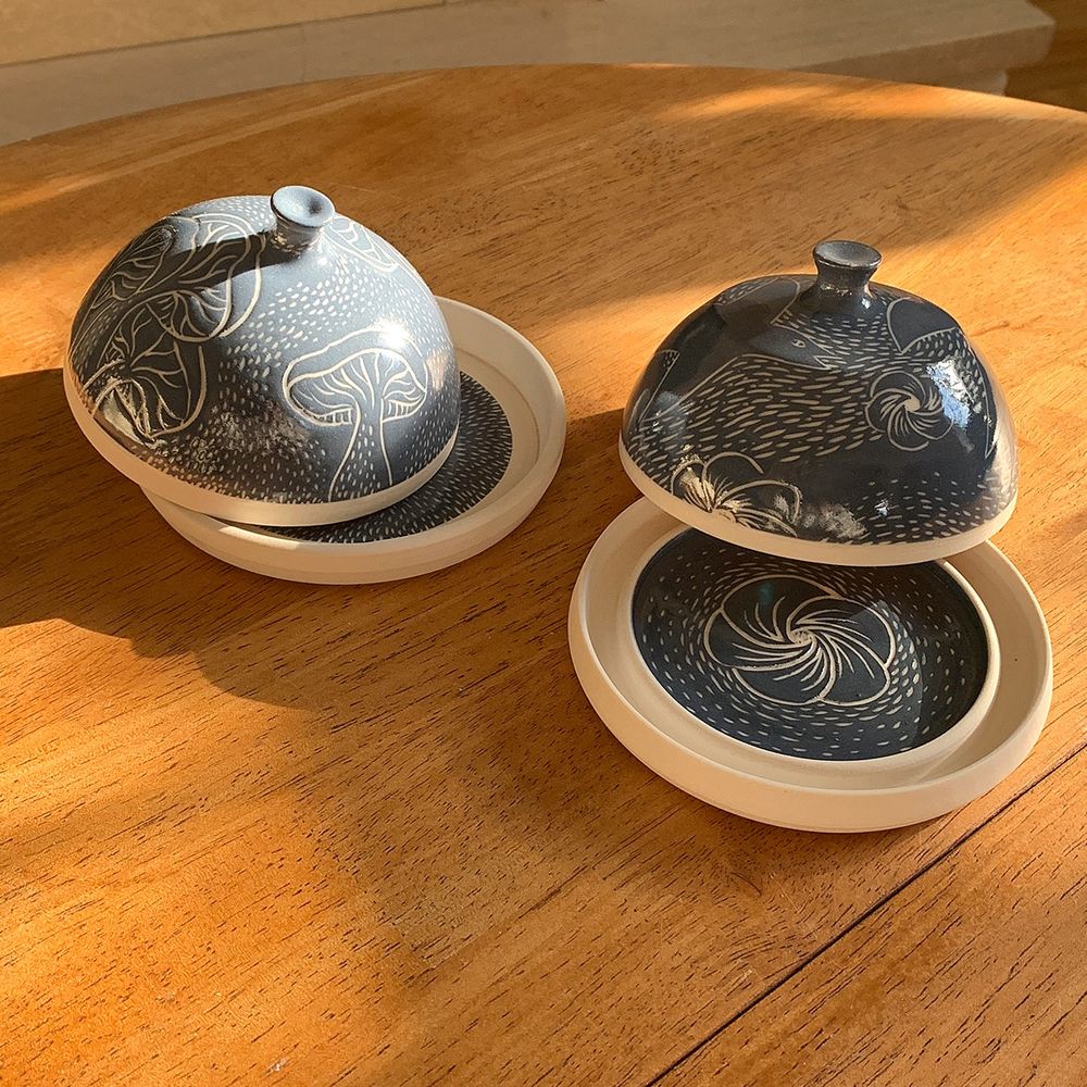 Two wheel thrown butter dishes, with blue-grey engobe on white clay, decorated using the sgraffito technique, with mushrooms, birds and flowers.