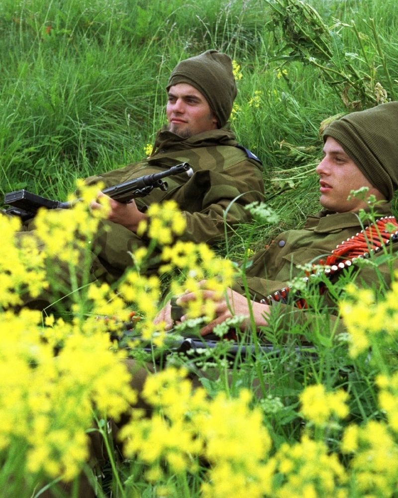 Et fargefoto av to uniformerte soldater som ligger på ryggen i en blomstereng. 