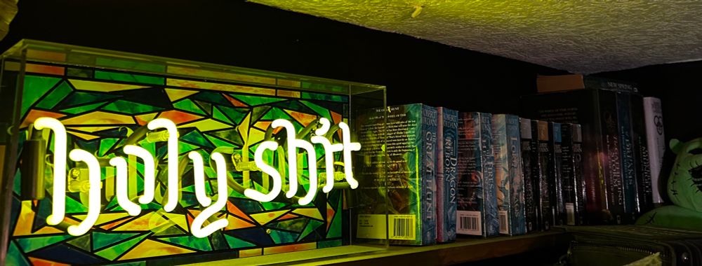 A neon sign spells “Holy Shit” and lights up. A stained glass effect background. 
To the right is a motley collection of the wheel of time book series in a mixture of paperback and hardback. 